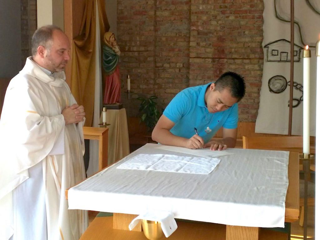 Frater James signs his vow renewal while Fr. David looks on.